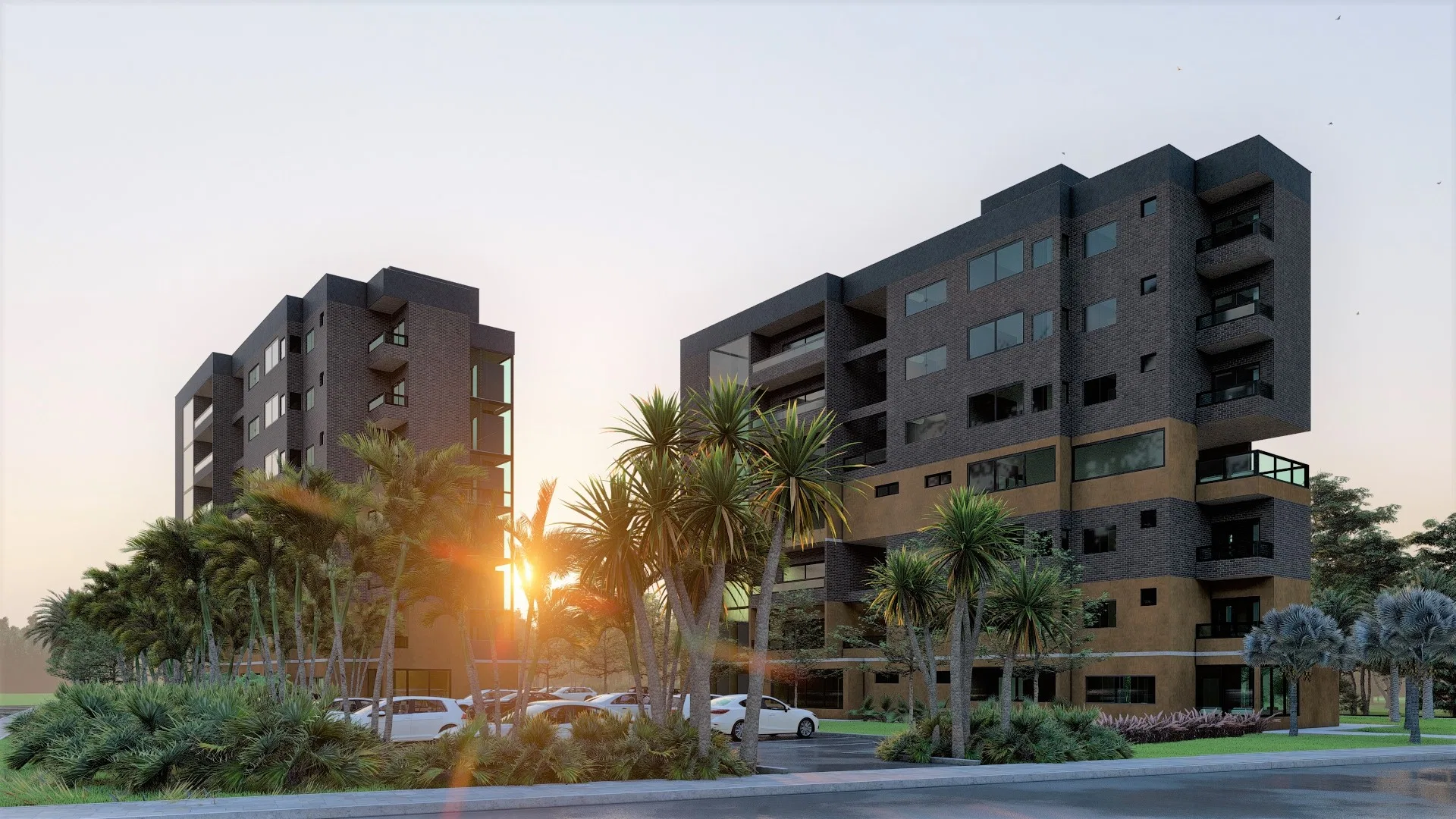 Duas torres residenciais em tijolo aparente ao entardecer, com faixas mostarda, varandas de vidro e o sol surgindo entre os volumes