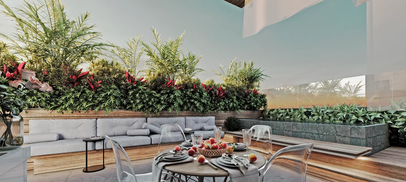 Terraço ao entardecer com sofá acolchoado cinza junto a canteiro de madeira com folhagem e cordiline vermelha, e mesa redonda posta com fruteira.